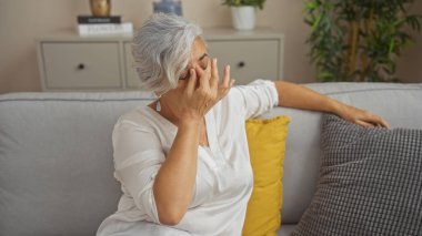Modern dekorları, yastıkları ve bitkileri olan rahat bir oturma odasında, bir koltukta otururken gözlerini ovuşturan kadın..