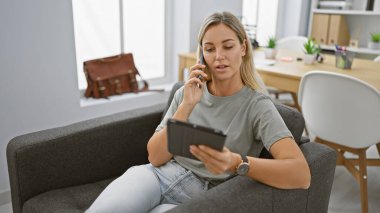 Genç bir kadın, modern bir ofis ortamında elinde tabletle bir telefon görüşmesi yapıyor..