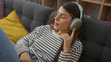Rahat İspanyol kadın, rahat bir oturma odasında kulaklıklarla müzik dinliyor..