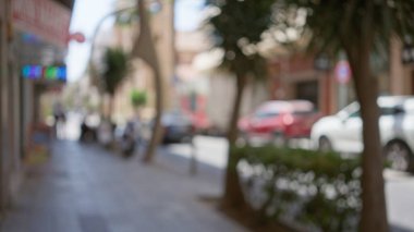Şehir sokakları bulanık. Odaklanamayan arabalar, ağaçlar ve binalar güneşli bir açık hava manzarası sergiliyor. Şehir merkezinde gezen insanlar ve canlı mağazalar..