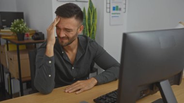 Ofis odasında bilgisayarında, bitkilerinde ve arka planında kitap yığınlarıyla hayal kırıklığı yaşayan sakallı yakışıklı İspanyol bir adam..