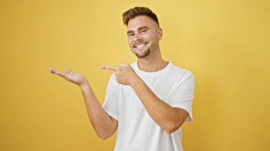 Sarı arka planda solu işaret eden sakallı yakışıklı genç bir adam, sıradan, dostane bir davranış sergiliyor..