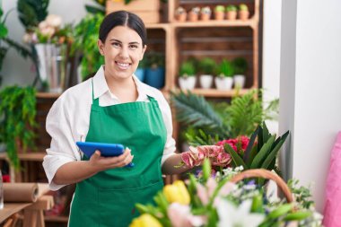Young beautiful hispanic woman florist smiling confident using touchpad at flower shop