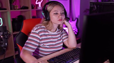 Kulaklıklı, renkli bir oyun odasında bilgisayar kullanan odaklanmış genç bir kadın..