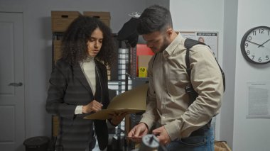 A man and woman, depicted as investigators, examine evidence in a cluttered police office environment. clipart