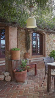 Terasotta tencereleri, kırsal bir bank ve gölgeli bir verandanın altında davetkar metal bir sandalye içeren huzurlu bir Akdeniz verandası..