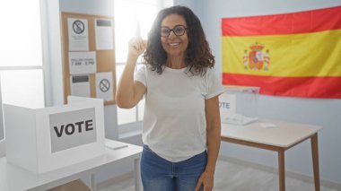 İspanyol seçmen odasında İspanyol bayrağıyla oy veren, gülümseyen ve parlak bir iç mekan gösteren bir kadın..