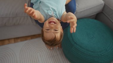 Küçük kız kapalı bir salonda oynuyor, baş aşağı ve gülümsüyor, neşeli, sevimli ve sevimli ifadelerle.