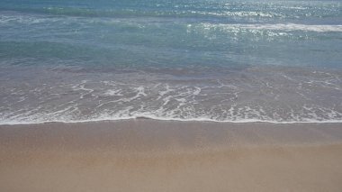 Prisitne sahil şeridi, yumuşak dalgalar, temiz bir gökyüzünün altında altın kumun üzerinde süzülüyor.