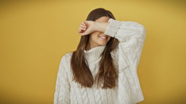 Beyaz kazaklı, gülümseyen genç bir İspanyol kadın, sarı bir arka planda, neşeyle gözlerini kapatıyor..