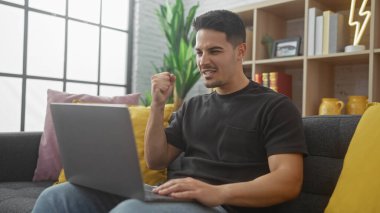 Sakallı genç İspanyol adam, samimi bir oturma odasında dizüstü bilgisayarla başarısını kutluyor..