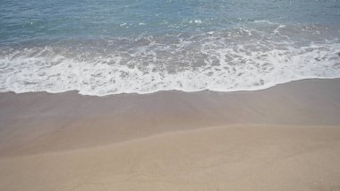 Kum kıyısı, berrak mavi gökyüzünün altında köpüklü okyanus dalgalarıyla karşılaşıyor