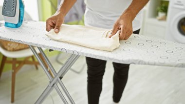 Parlak bir çamaşırhanede ütü yapan İspanyol bir adam ütü masasındaki kumaşa odaklanıyor..