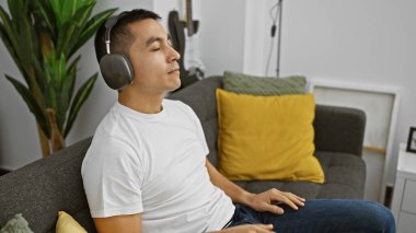 Gevşemiş bir İspanyol, modern bir oturma odasında, sakin bir ortam yayarak, kulaklıkla müzik dinlemekten hoşlanır..