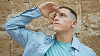 Genç bir İspanyol adam güneşli bir şehir sokağında gözlerini güneşten korur ve portresinden gündelik ve çekici bir hava yayar..