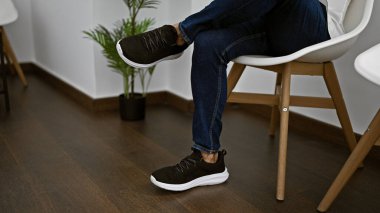 Man in modern office waiting area with crossed legs showcasing casual shoe style against minimalist decor. clipart