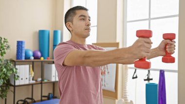 Genç, yetişkin bir İspanyol adam, dambıllarıyla kapalı bir rehabilitasyon kliniğinde egzersiz yapıyor..