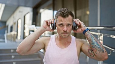 Sakallı ve dövmeli genç bir İspanyol şehir caddesinde kulaklıklarını düzeltiyor..