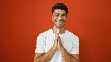 Sakallı, beyaz tişörtlü neşeli genç bir adam izole edilmiş kırmızı arka plana karşı şükranlarını ifade ediyor..