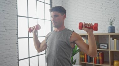 Parlak bir iç mekanda halterlerle egzersiz yapan yakışıklı bir adam. Formda ve sağlıklı bir yaşam tarzı sergiliyor..