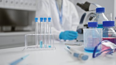Laboratuvar önlüğü ve eldiven giyen odaklanmış bir bilim adamı iyi donanımlı bir laboratuarda deneyler yapıyor.