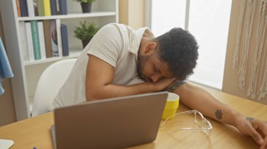 Yorgun bir Afrikalı adam dizüstü bilgisayarın yanında dinleniyor..