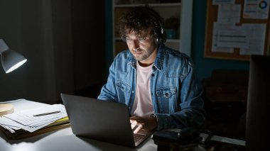 Odaklanmış İspanyol adam geç saatlere kadar masa lambası altında dizüstü bilgisayar kullanarak çalışıyor. Profesyonelliği yansıtıyor..