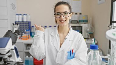 Laboratuvar ortamında bilimsel ekipmanlarla çevrili, laboratuvar önlüklü gülümseyen İspanyol kadın..