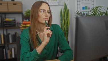 Ofis ortamında genç, çekici, sarışın bir kadın modern bir iş yerindeki bilgisayar ekranına dalgın dalgın bakıyor..