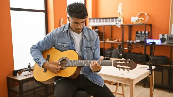 stock image Handsome hispanic man playing guitar in a music studio with recording equipment