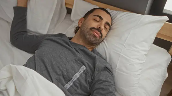 stock image Handsome man with moustache sleeping peacefully on a bed in a cozy bedroom with white pillows and wooden headboard