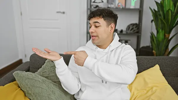 stock image Young man presenting with hand in a modern living room, showing casual style, indoor setting, and comfort.