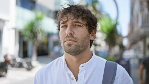 Stock image A handsome, green-eyed, bearded hispanic man in a casual shirt standing outdoors on an urban city street.