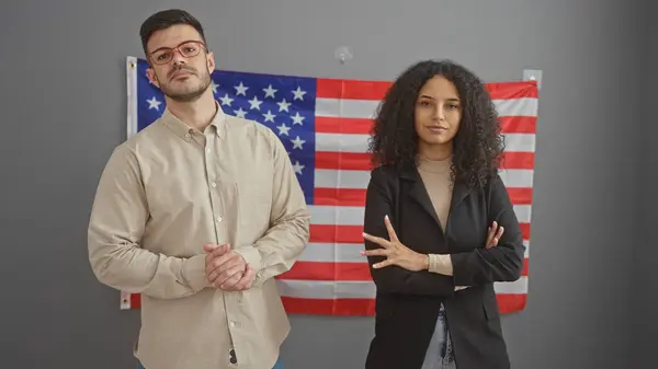 stock image Confident man and woman posing in an office with the united states flag, representing leadership and professionalism