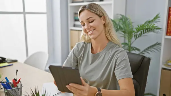 stock image Smiling woman using tablet in modern office with plants and desk accessories.