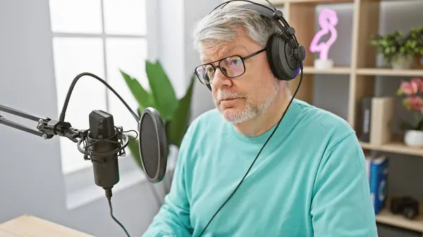 stock image A mature man with grey hair in a radio studio wearing headphones, speaking into a microphone.