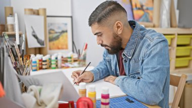 Yaratıcı bir stüdyo ortamında etrafı sanat malzemeleriyle çevrili ev resimleriyle çevrili bir adam..