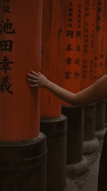 Genç bir kadının saygıdeğer yürüyüşü, yürüyüşü ve geleneksel Japon torii kapılarına dokunuşu Fushimi inari-taisha, turuncu, ahşap yol boyunca ilerlerken geriye doğru bir bakış.
