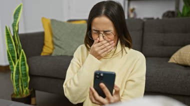 İspanyol bir kadın telefonunda bir mesaj okuyor. Kapalı bir kanepede oturuyor. Dekor geçmişi var..