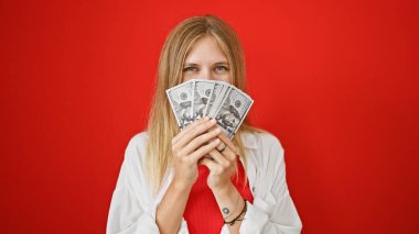 Sarışın, ağzı kapalı, çekici bir genç kadın. Kırmızı arka planda dolarlar var..