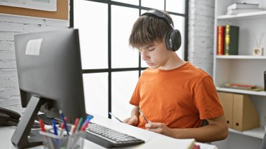 Genç sarışın bir çocuk modern, parlak bir sınıf ortamında dikkatlice bilgisayarının başında çalışıyor..