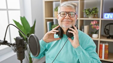 Radyo stüdyosunda kulaklıklarla gülümseyen son sınıf öğrencisi medya prodüksiyonu ve yayın yapıyor..