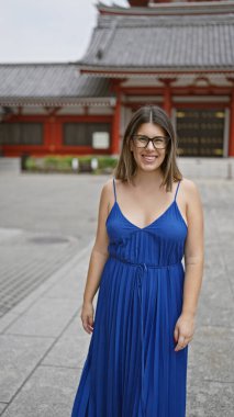 Gülümseyen ve neşeli, gözlüklü güzel İspanyol kadın Tokyo 'daki sembolik senso ji türbesine özgüvenle poz veriyor, doğal güzellik ve kaygısız mutluluk yayıyor.