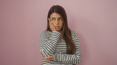 Çizgili tişörtlü düşünceli genç bir İspanyol kadın pembe izole bir arka plana karşı poz veriyor..