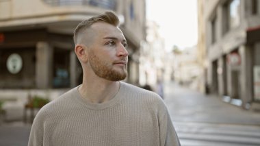 Sıradan giyinmiş sakallı yakışıklı genç adam boş bir caddede düşünceli bir şekilde dikiliyor..