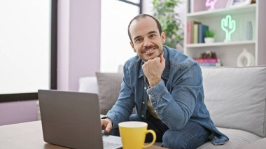 Samimi oturma odasında dizüstü bilgisayarda çalışan sakallı İspanyol bir adam..
