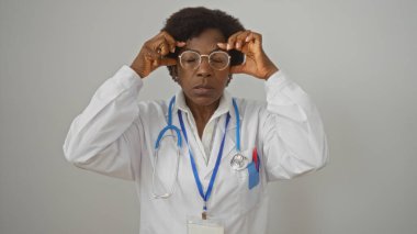 Orta yaşlı, kıvırcık saçlı bir kadın doktor baş ağrısı çekiyor, gözlerini kapıyor ve şakaklarına dokunuyor.