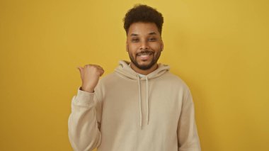 Yakışıklı bir adam, parlak sarı bir arka plana başparmağıyla işaret ediyor. Kendine güveni ve yaklaşımı var..