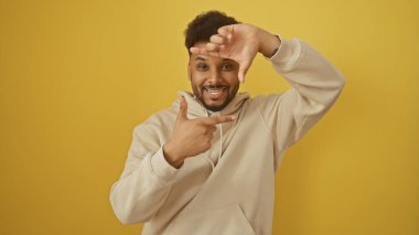 Neşeli adam yüzünü çerçeveliyor, parmakları sarı arka planda.