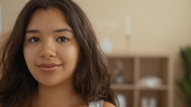 Güzel, esmer, genç, İspanyol bir kadın sakin bir spa odasında gülümsüyor. Kapalı mekandaki güzellik ve güzelliği vurguluyor..